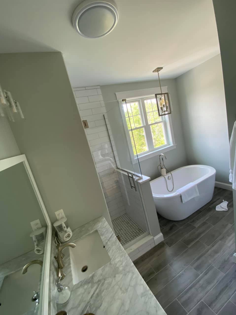 Bathroom featuring a freestanding white tub, glass shower, and dark wood-look floor in Sodus, NY