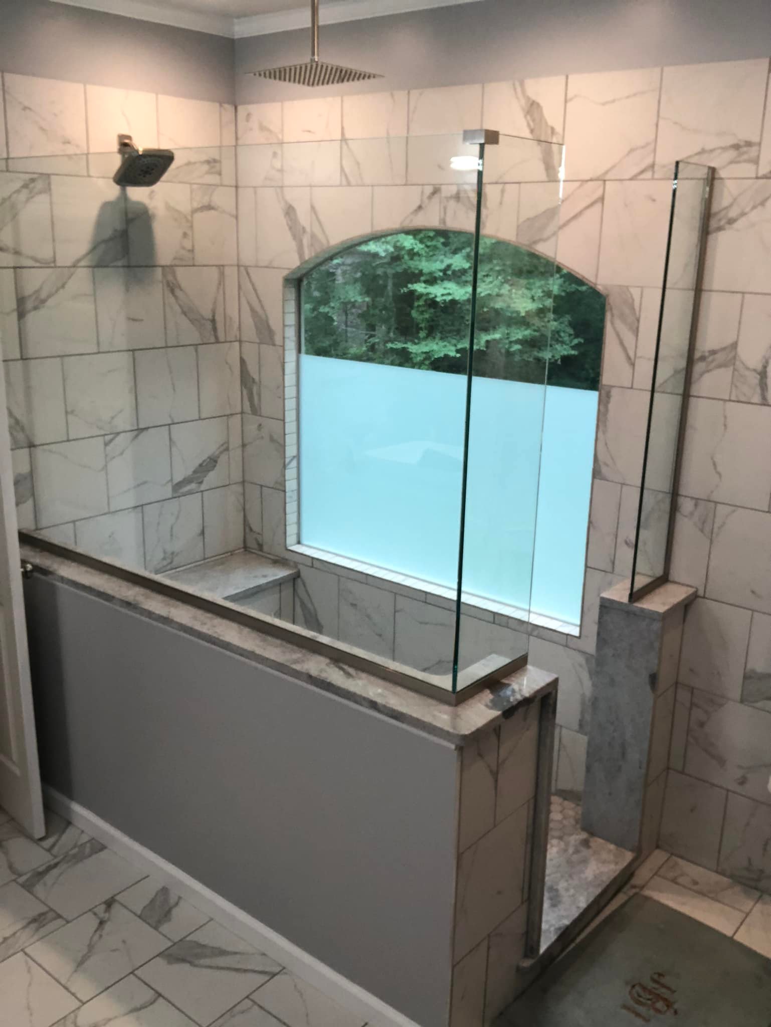 Tiled shower area with a glass enclosure and a window with frosted glass in Lyons, NY