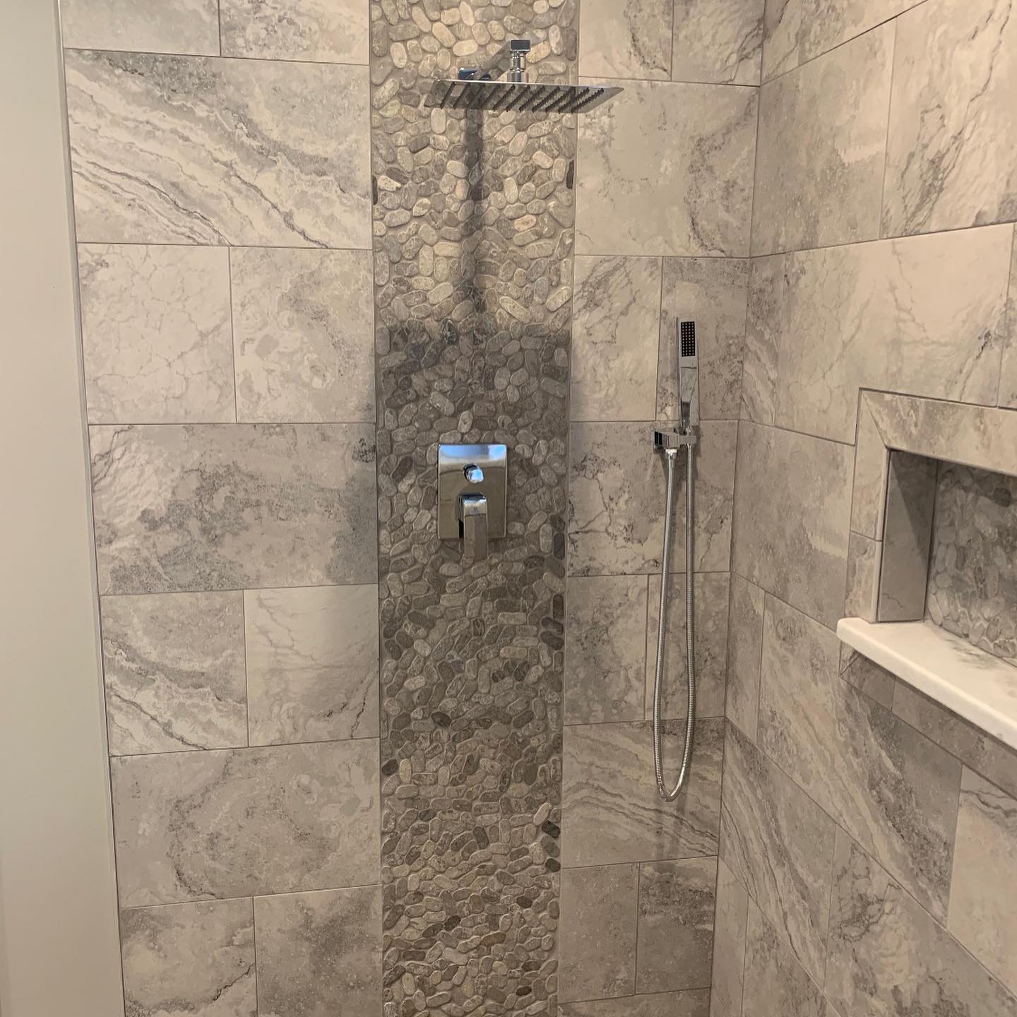 Shower wall with large gray tiles and a vertical accent strip of circular stones in Sodus, NY