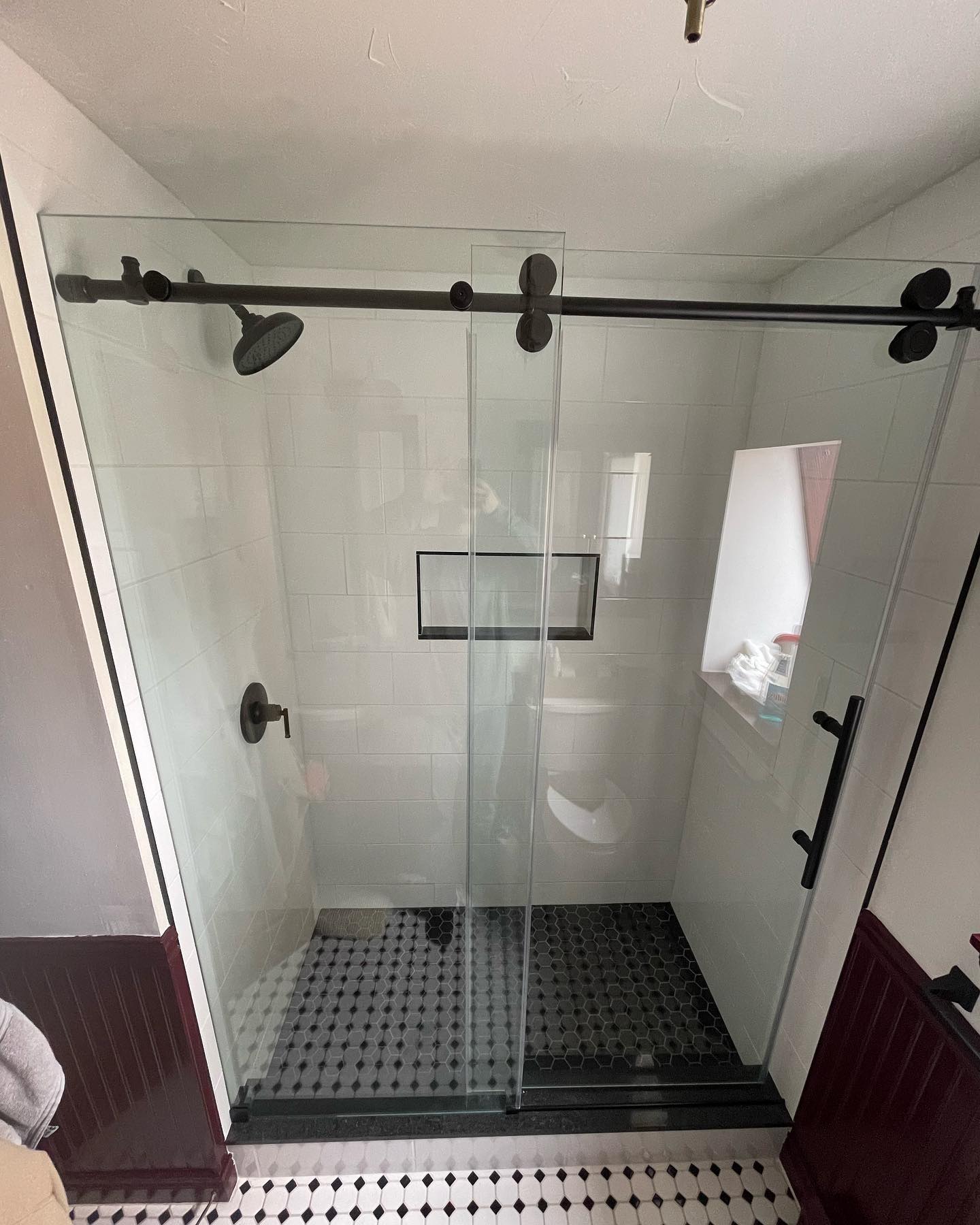 Shower stall with a black sliding glass door, white wall tiles, and black fixtures in Savannah, NY