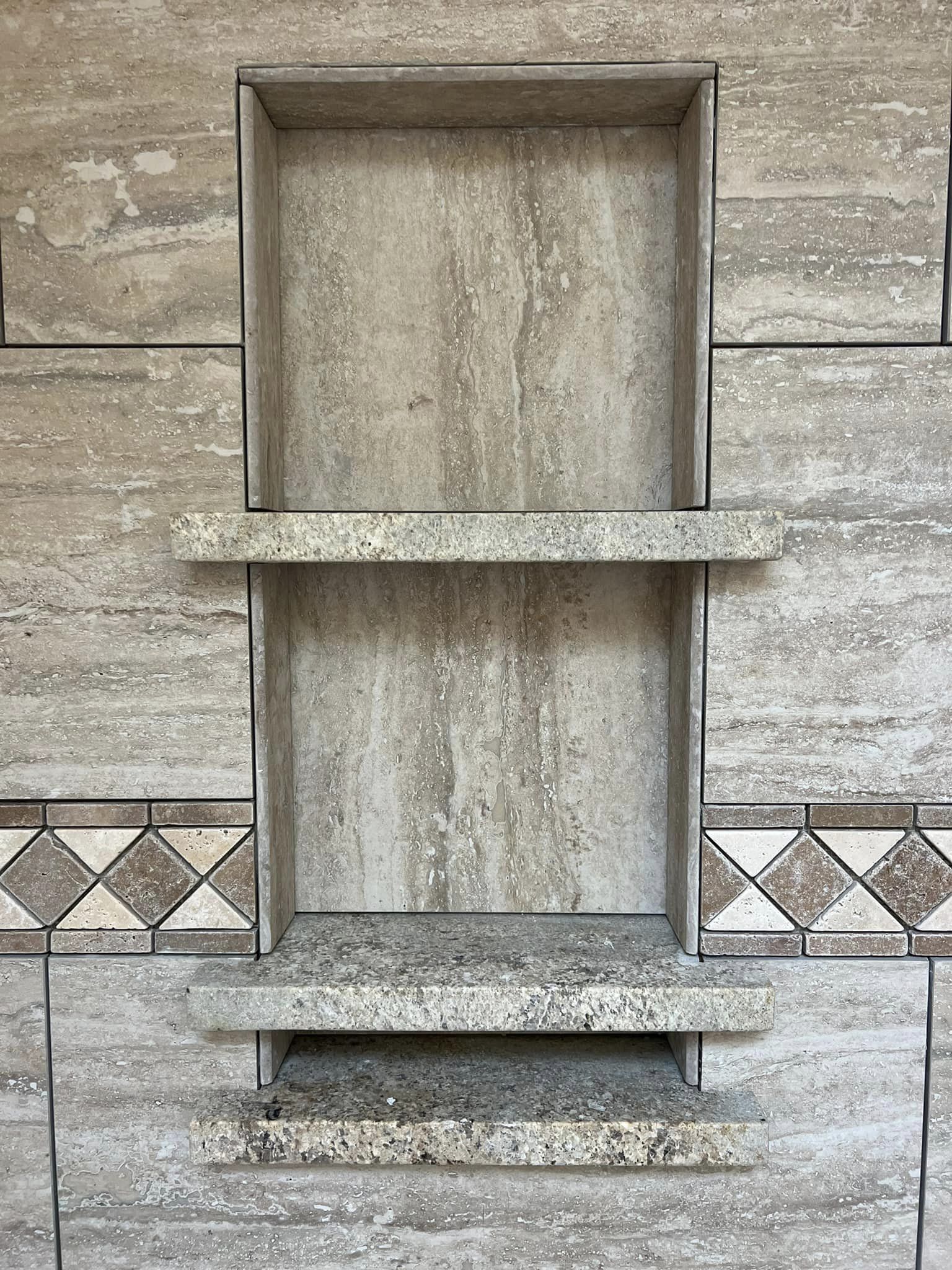 Built-in double shower niche featuring stone shelving and decorative border tiles in Oswego, NY