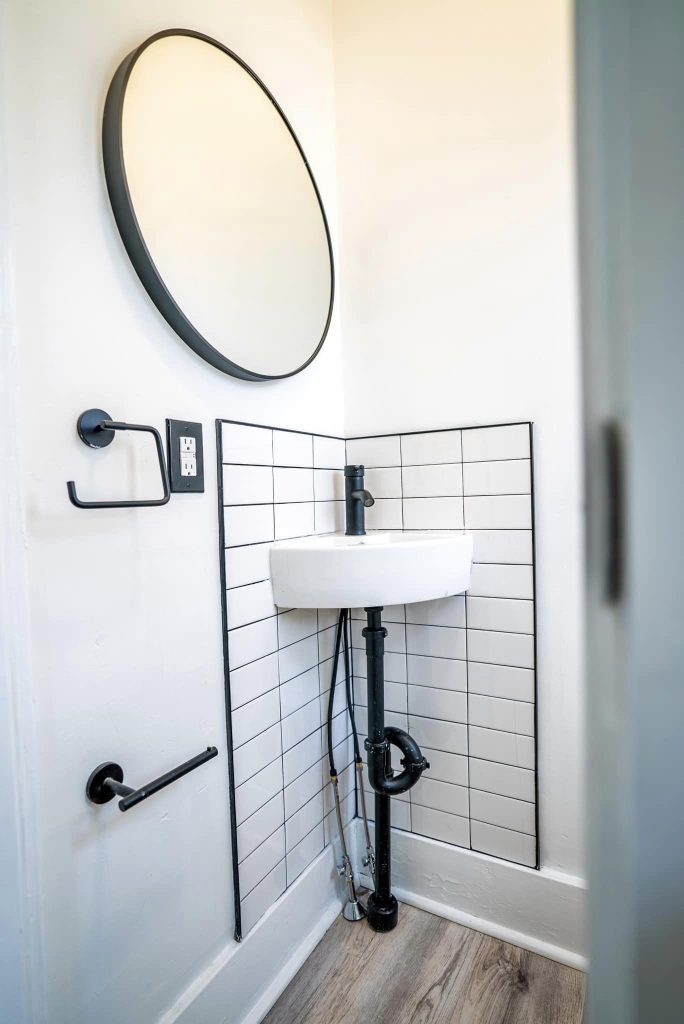 Small bathroom with a wall-mounted pedestal sink and black tile accent in Fair Haven, NY