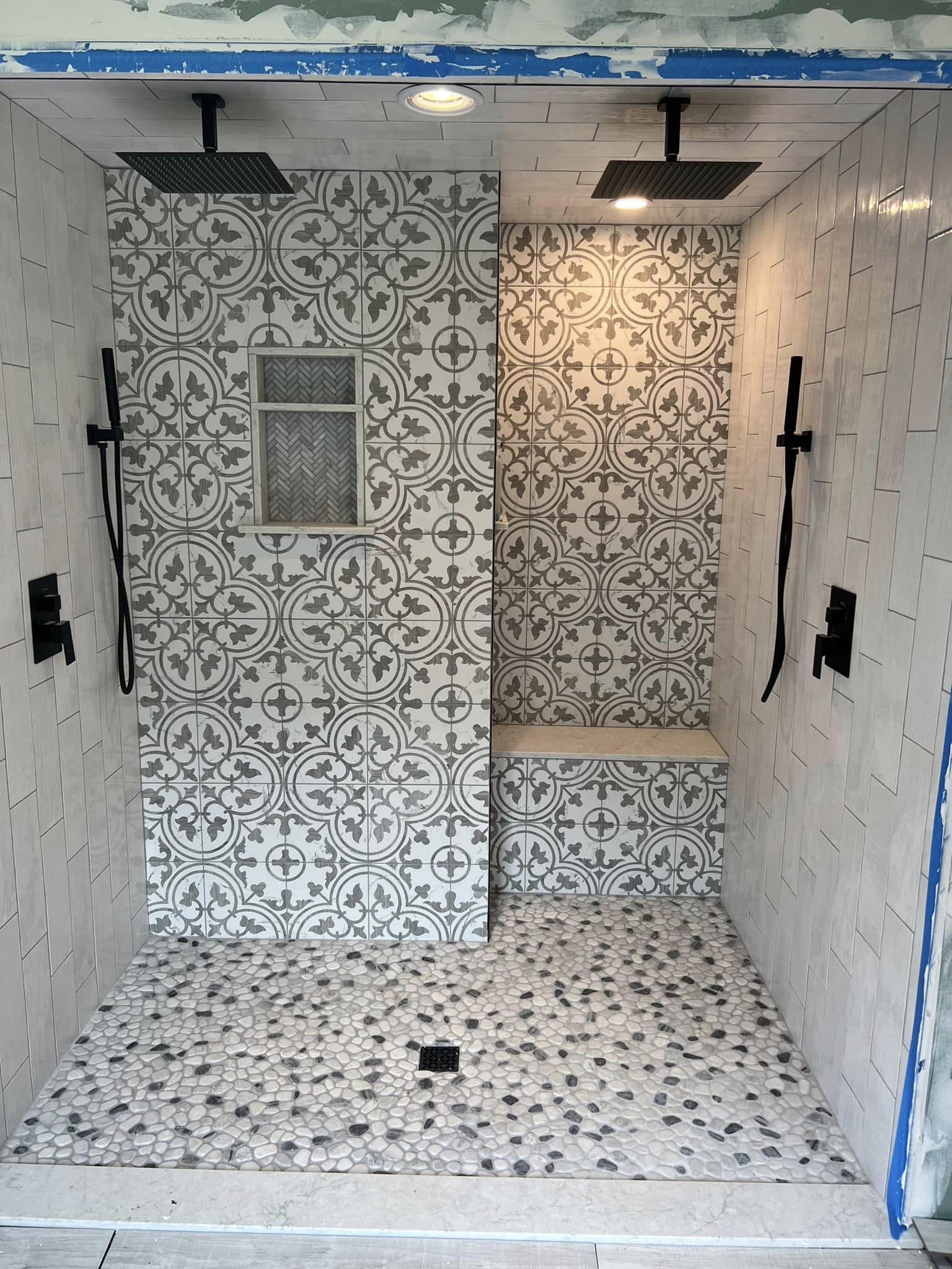 Walk-in shower featuring patterned tile walls, dual shower heads, and a corner bench in Williamson, NY
