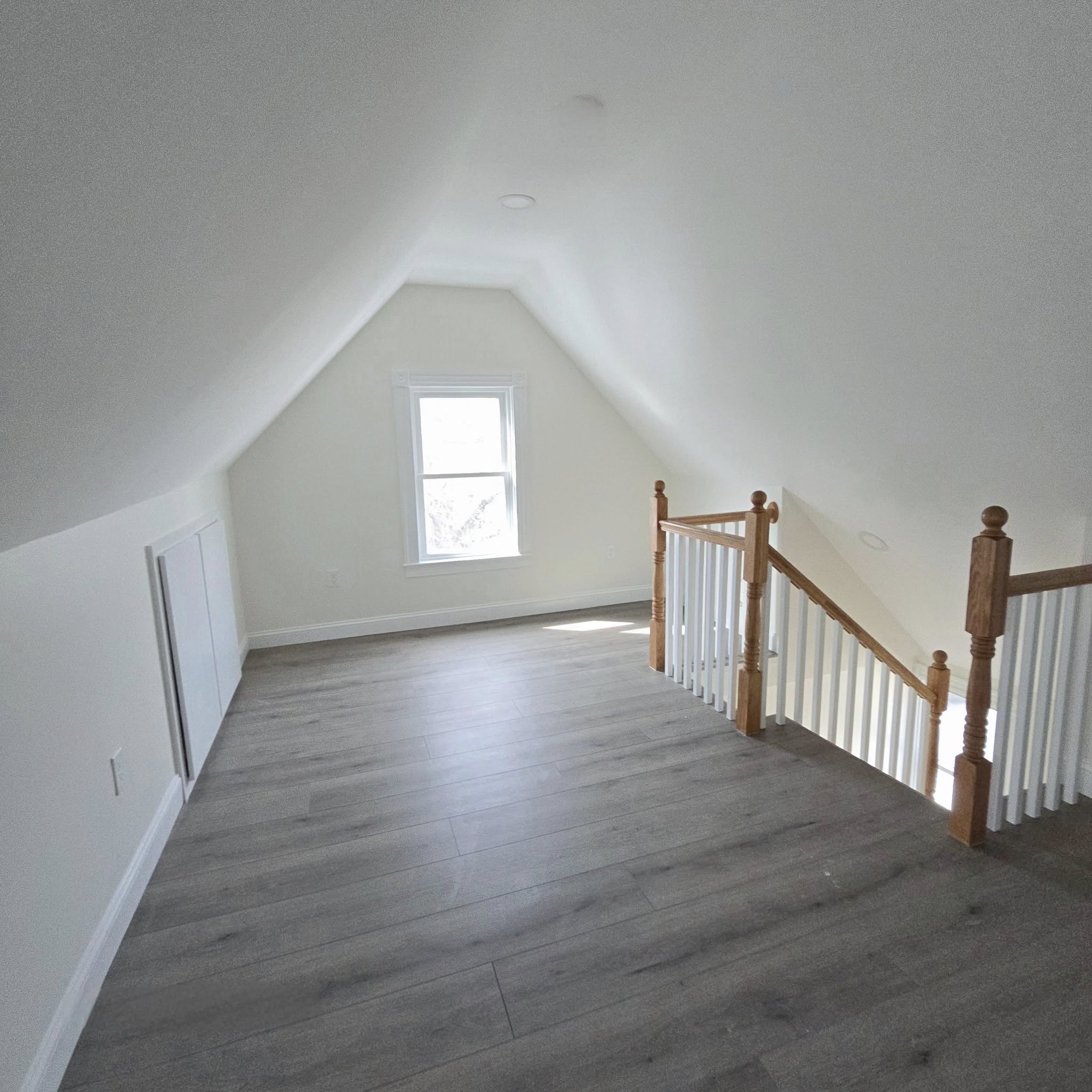 Empty finished room featuring sloped ceilings, wooden staircase, and gray laminate flooring in Palmyra, NY