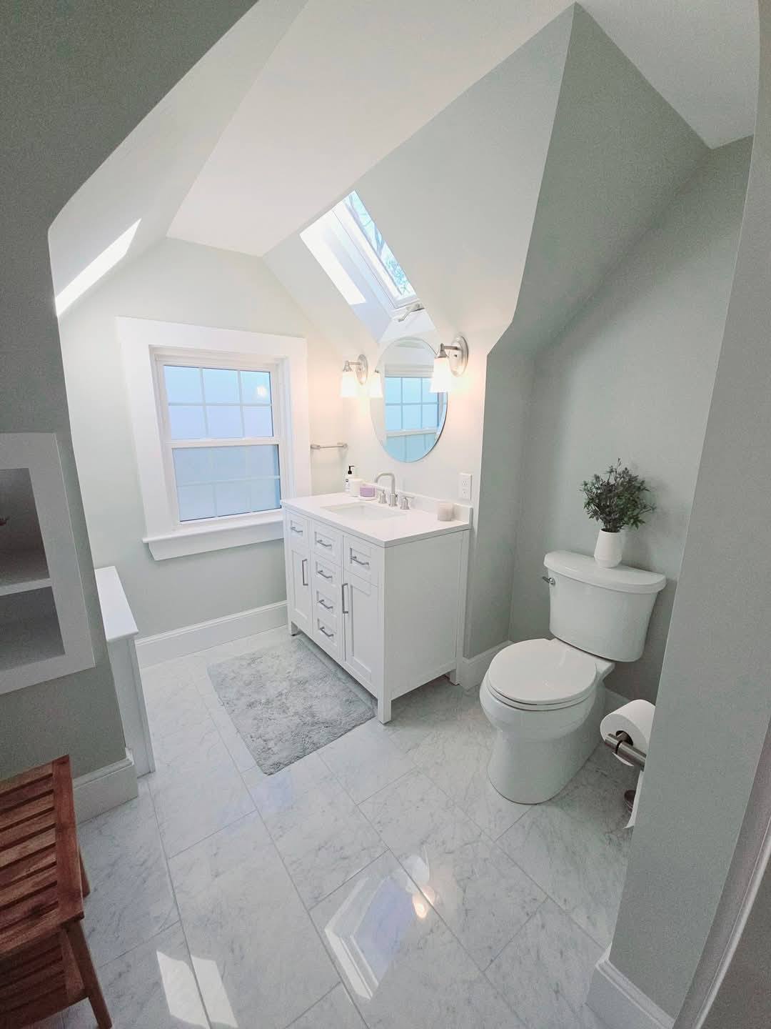 Small bathroom with sloped ceiling, white vanity, toilet, and marble floor tiles in Fair Haven, NY