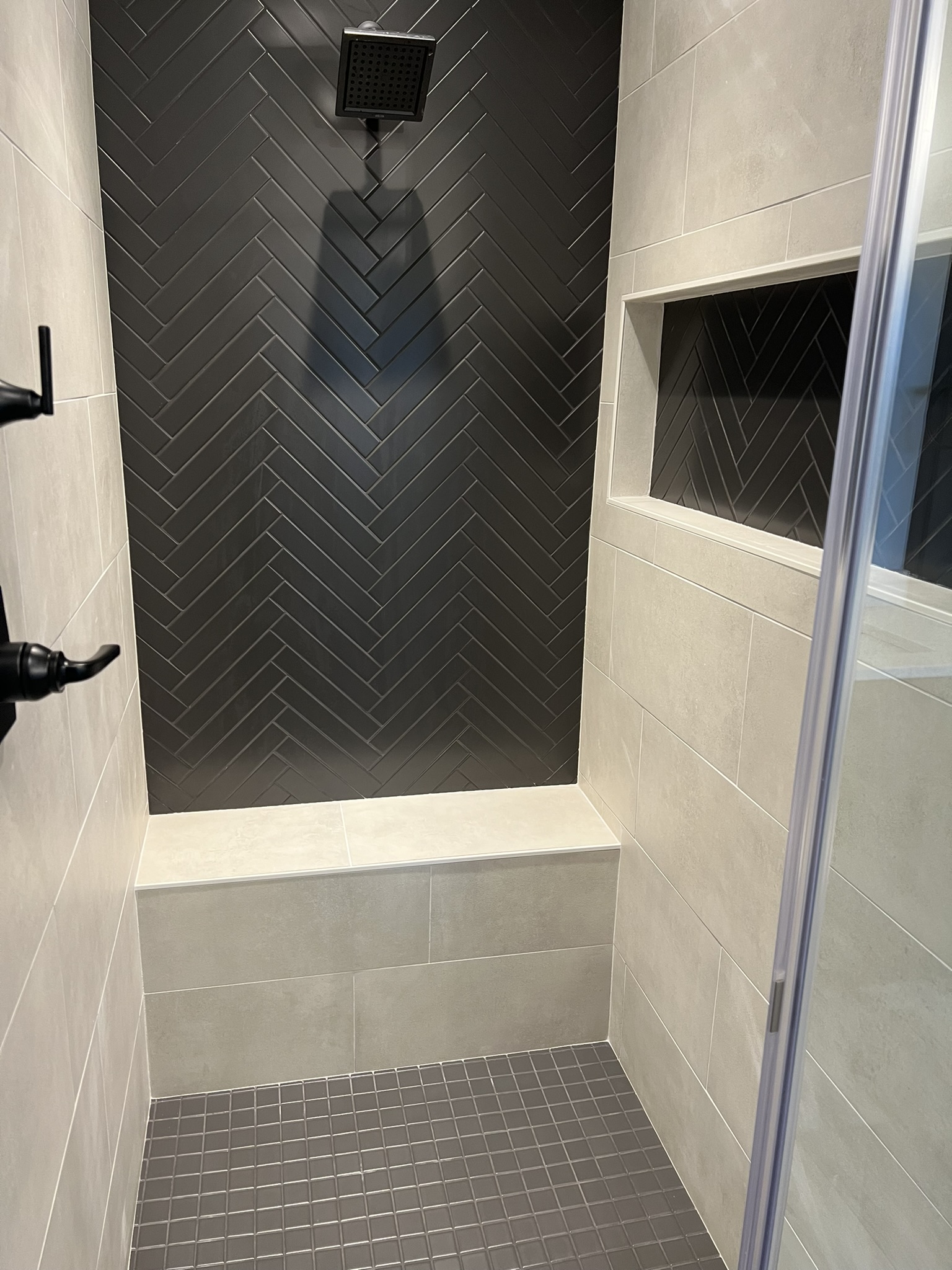 Walk in shower with dark herringbone tile wall and built in bench