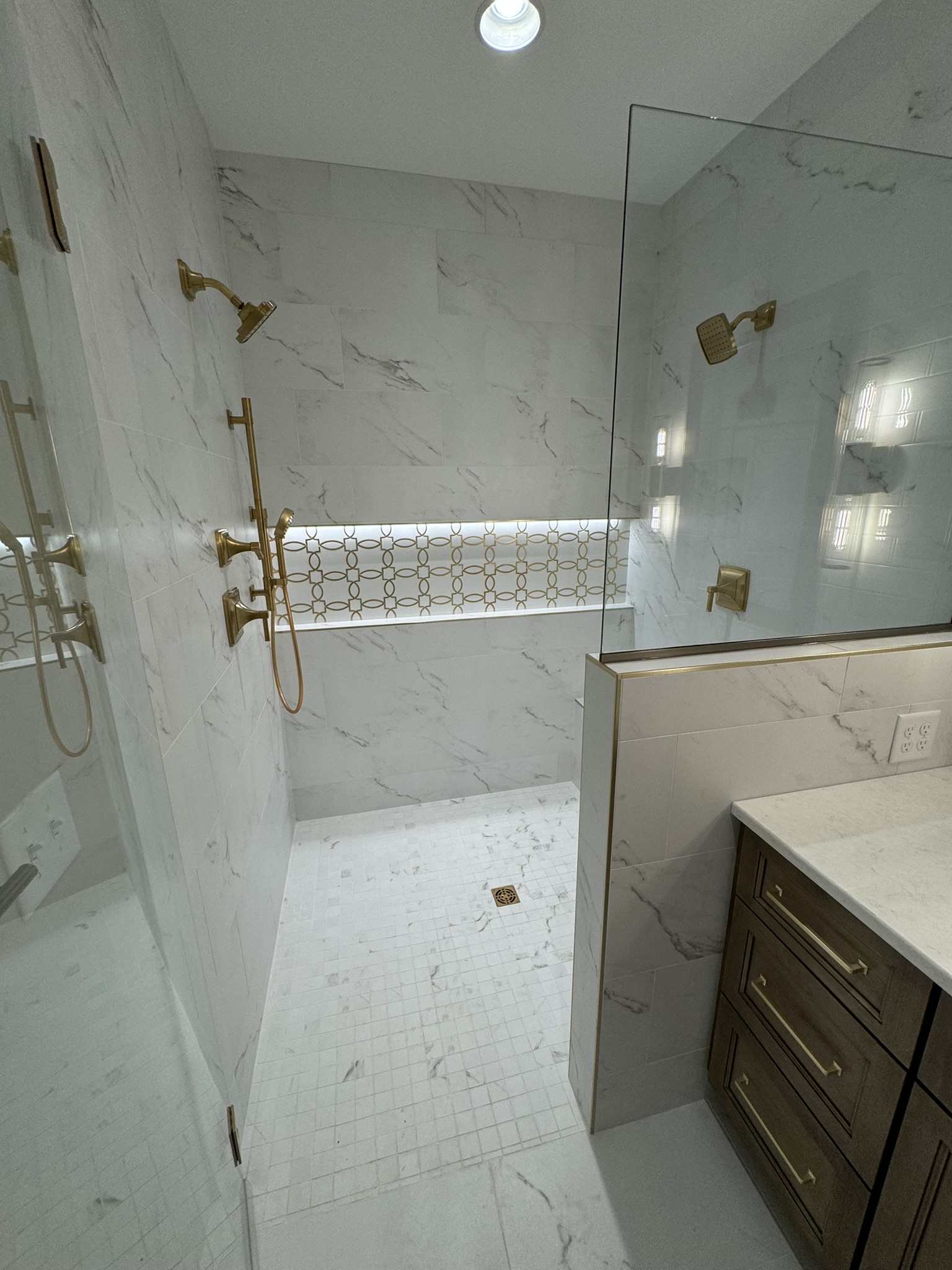 Walk in shower with white marble tile, gold fixtures and glass door in Fair Haven, NY
