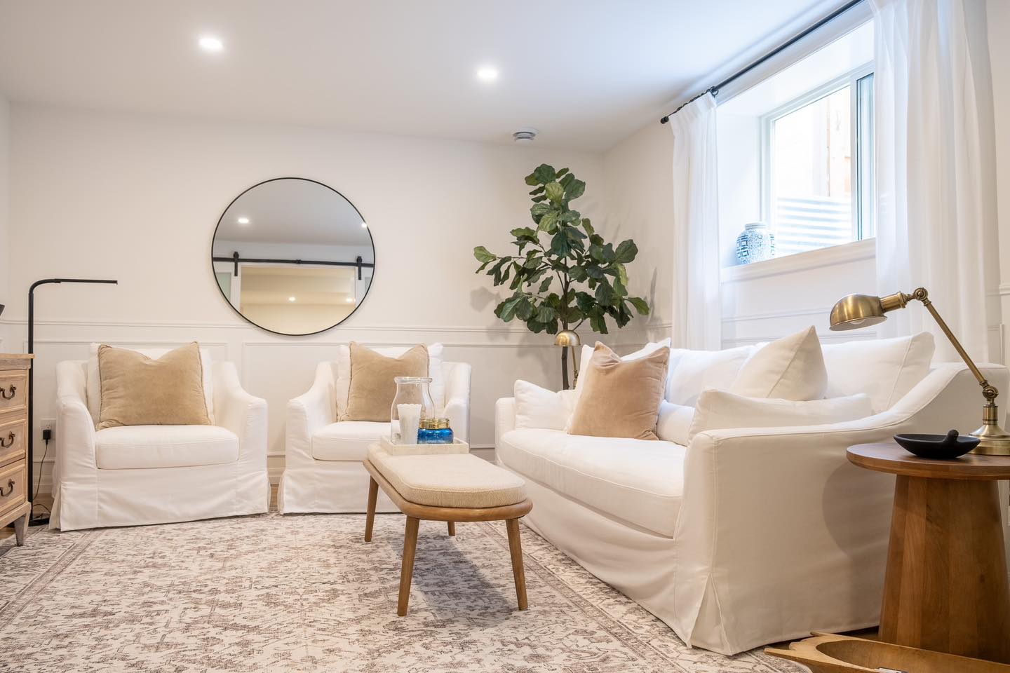 Sitting area featuring white sofa, matching armchairs, coffee table, and a round wall mirror in Savannah, NY