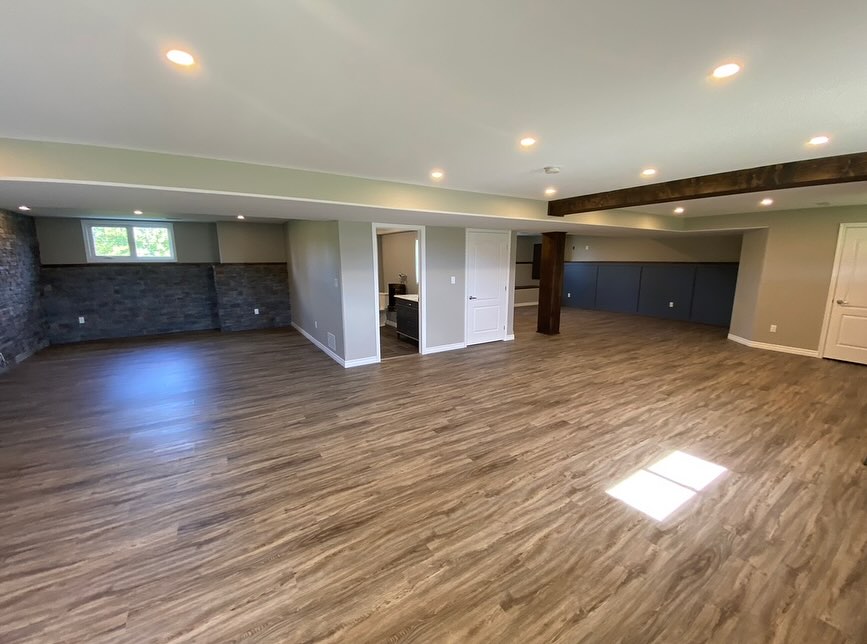 Basement living area with wood floor, gray wall paneling, and stone accents in Walworth, NY