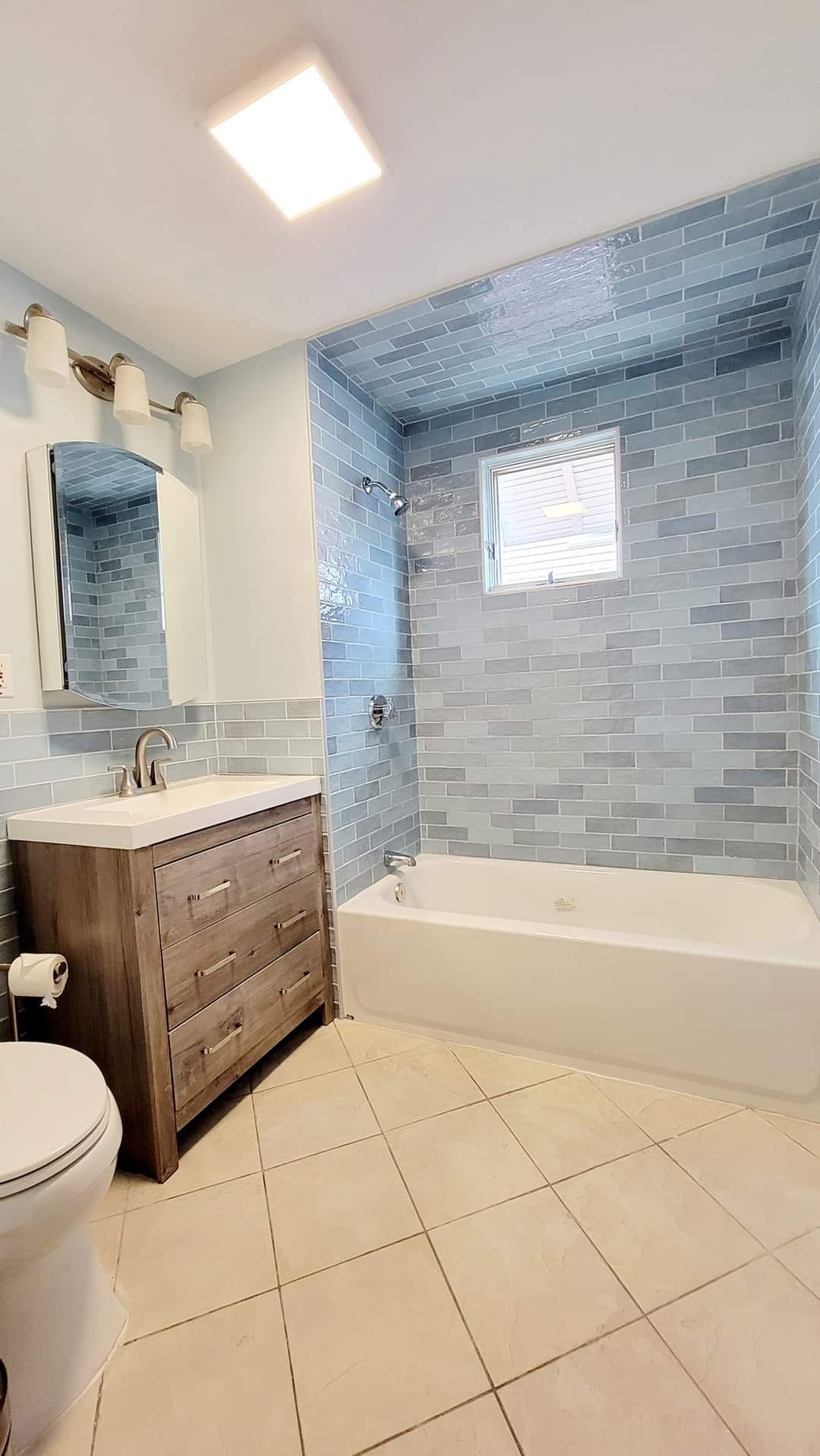 Bathroom with blue subway tile wall around a bathtub and wooden vanity in Newark, NY