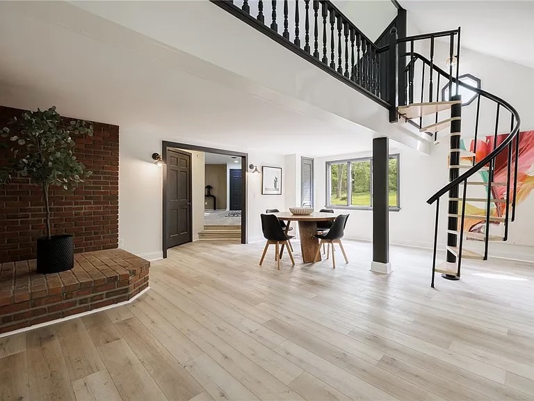 Open living area with wood flooring, brick fireplace, and black spiral staircase in Savannah, NY
