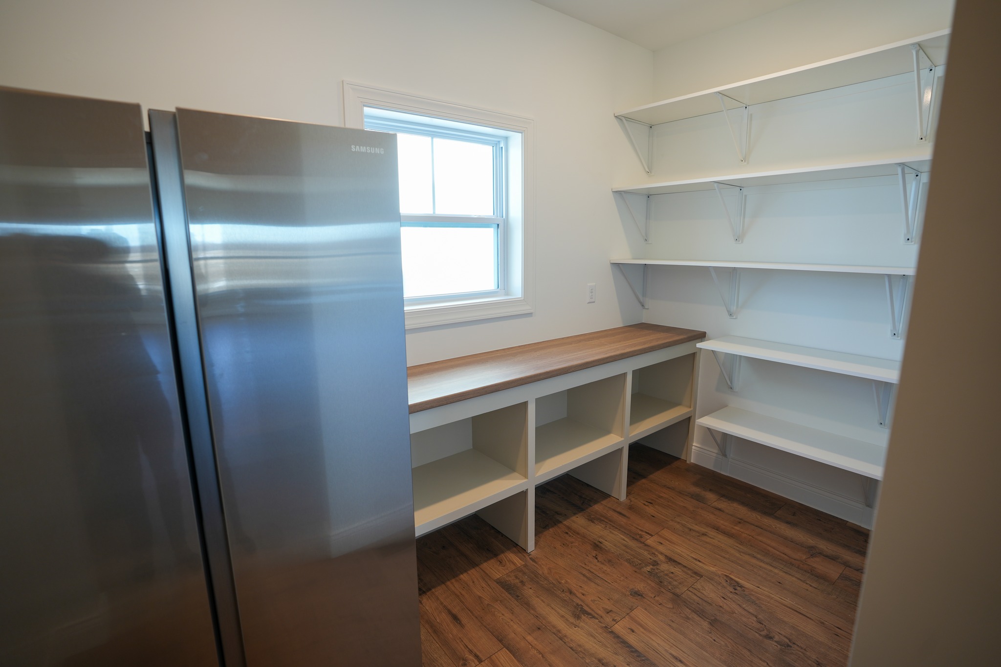 Pantry room with stainless steel refrigerator and open white shelves above wooden counter in Fulton, NY