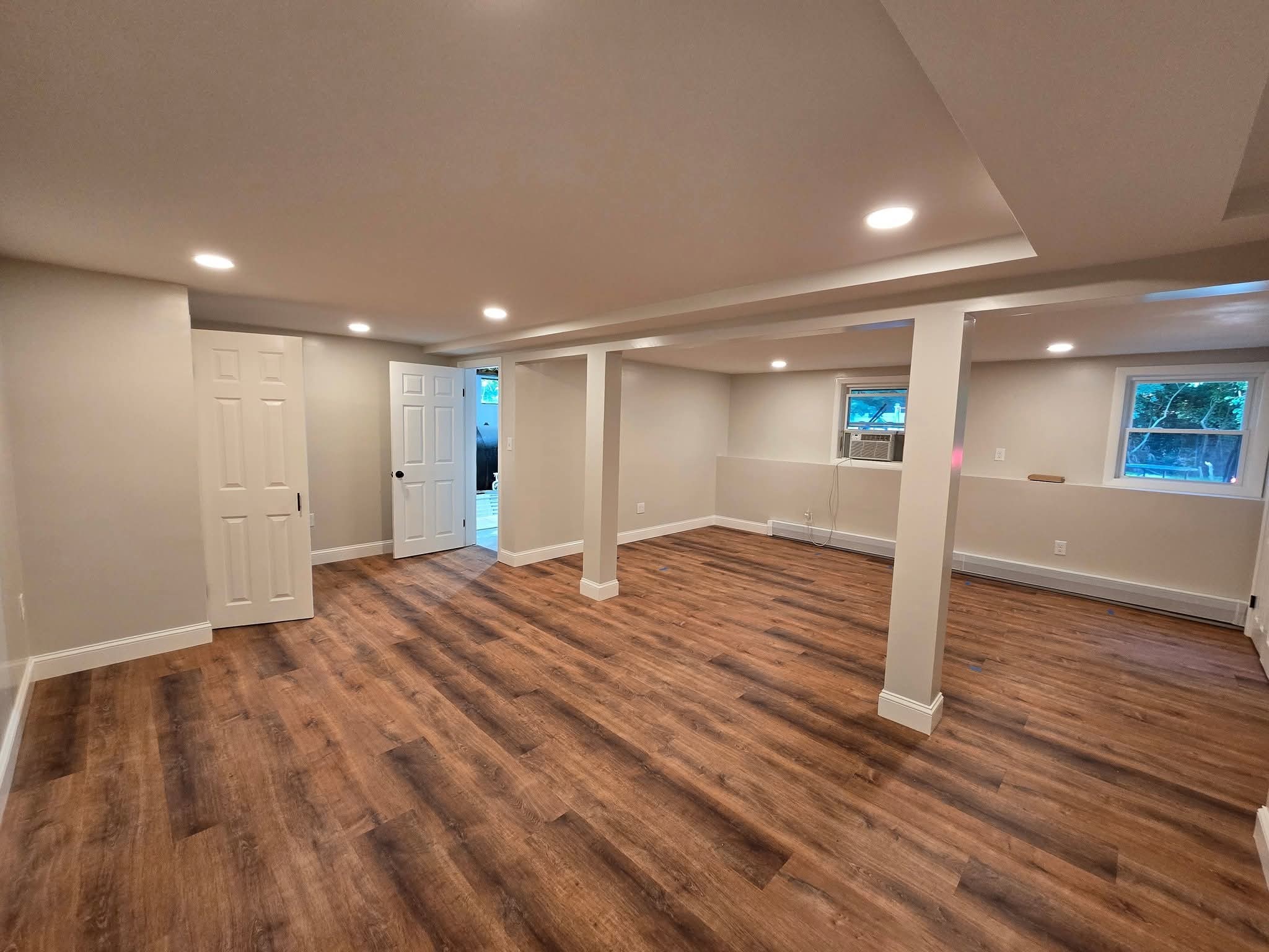 Open basement living area featuring neutral walls, wood plank flooring, and support pillars in Macedon, NY