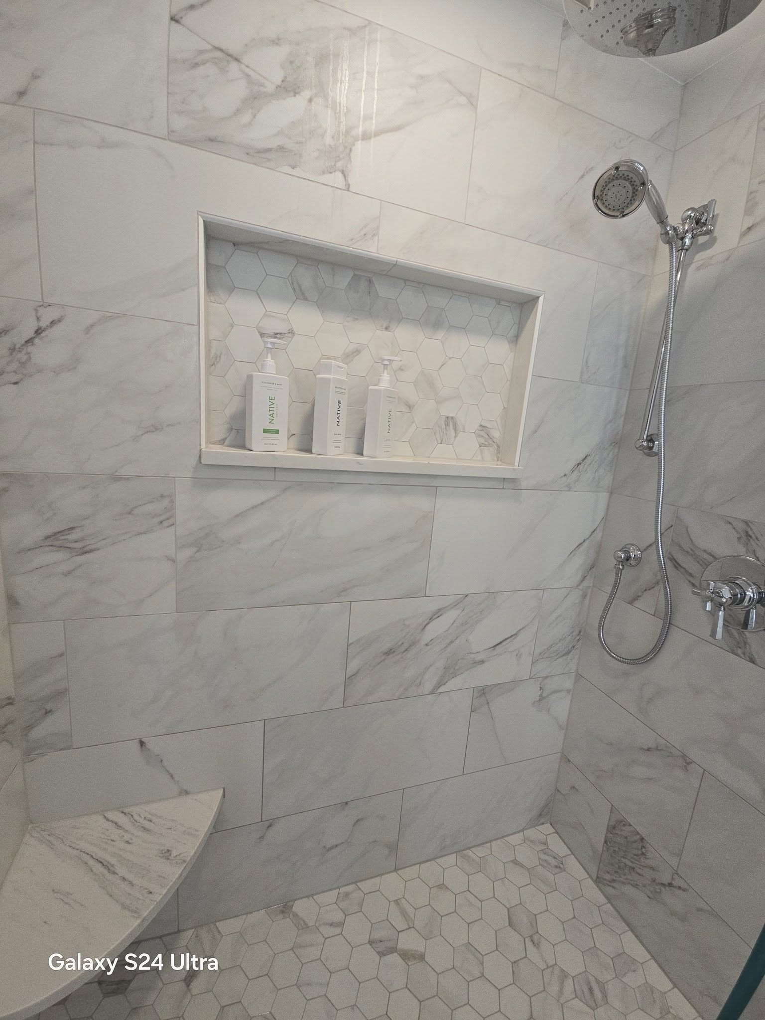 Shower stall with white marble wall tiles and a small recessed storage shelf