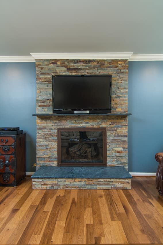 Fireplace surrounded by stacked stone tiles with a mounted television above it in North Rose, NY